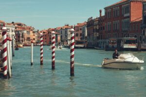 A serene view of a motorboat cruising past iconic striped poles on Venice's Grand Canal.