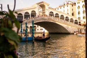 A gondola navigates the Grand Canal with Rialto Bridge lit by the setting sun in Venice, Italy.