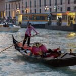 A gondolier navigates a gondola on a Venetian canal in the evening light, offering a glimpse of traditional Venice.